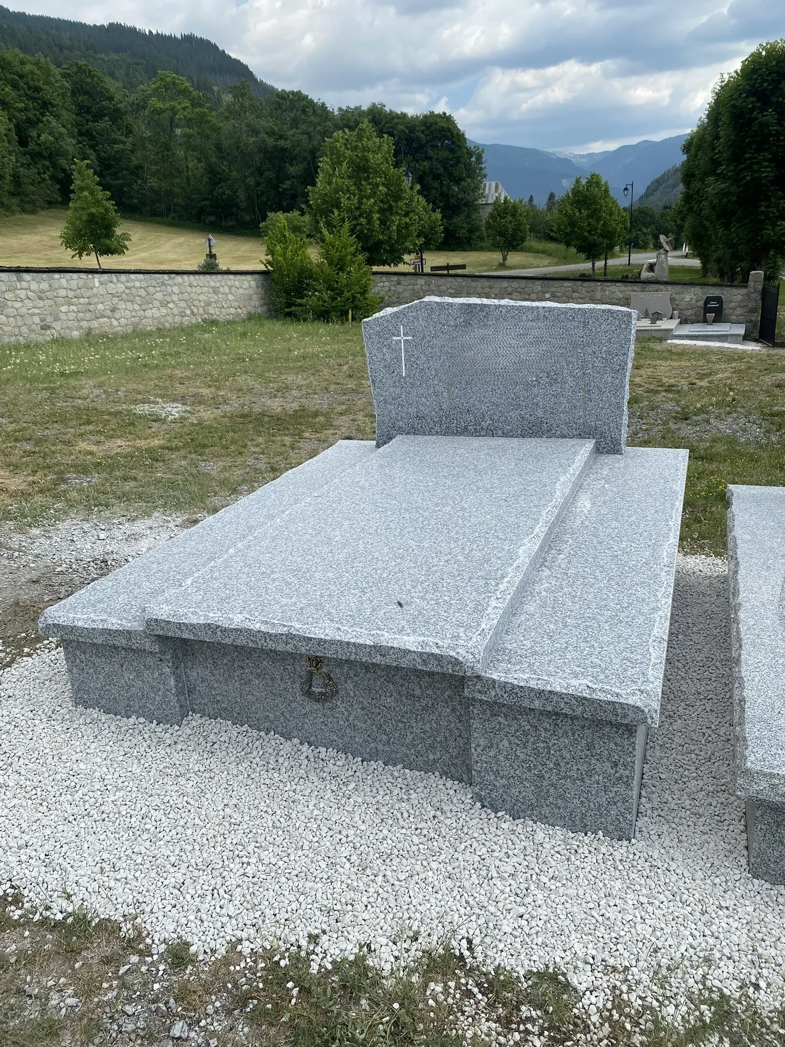 Tombe simple en granit gris installée dans un cimetière de montagne.