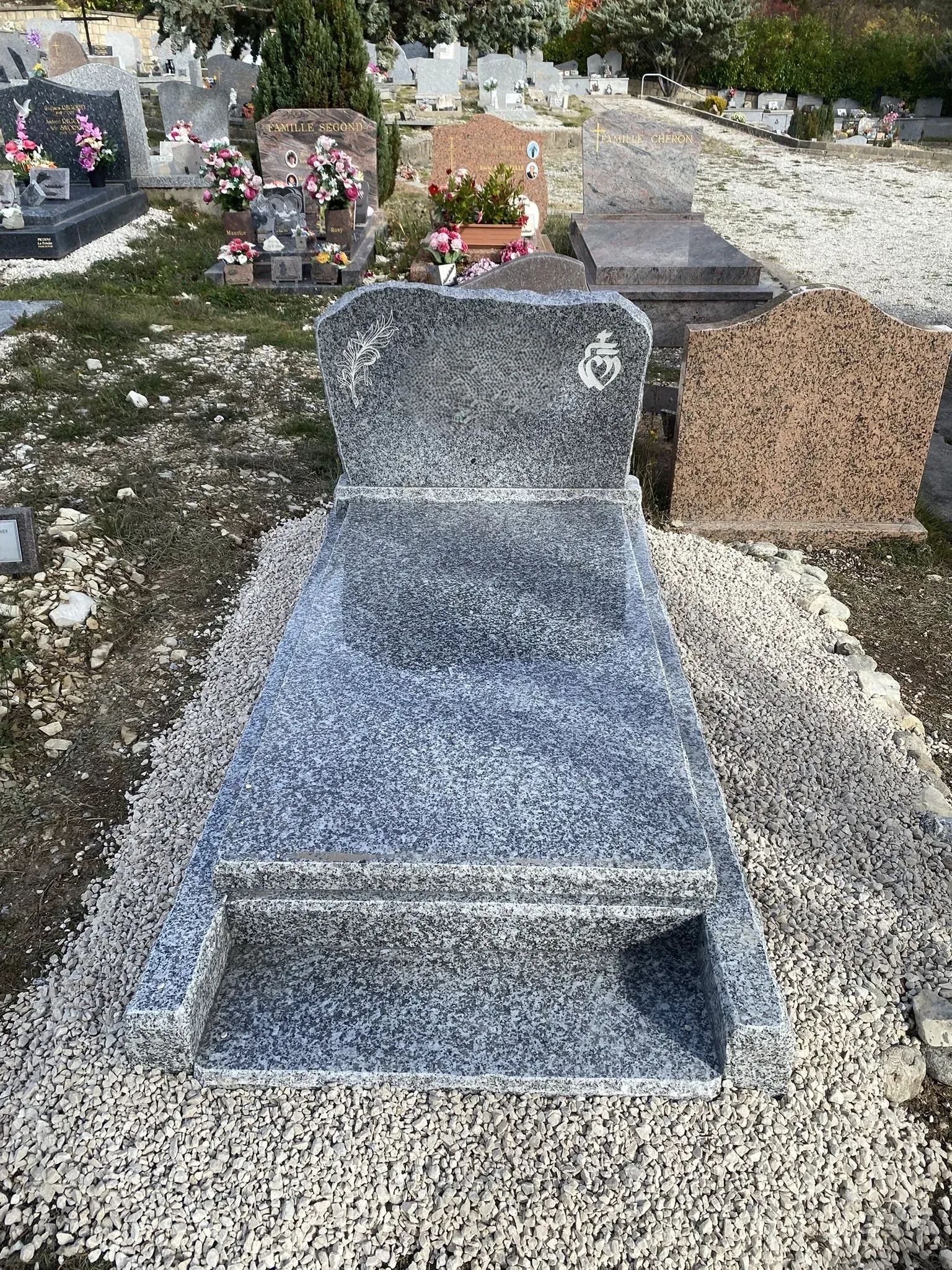 Concession funéraire en granit gris bleuté entourée de gravillons blancs.