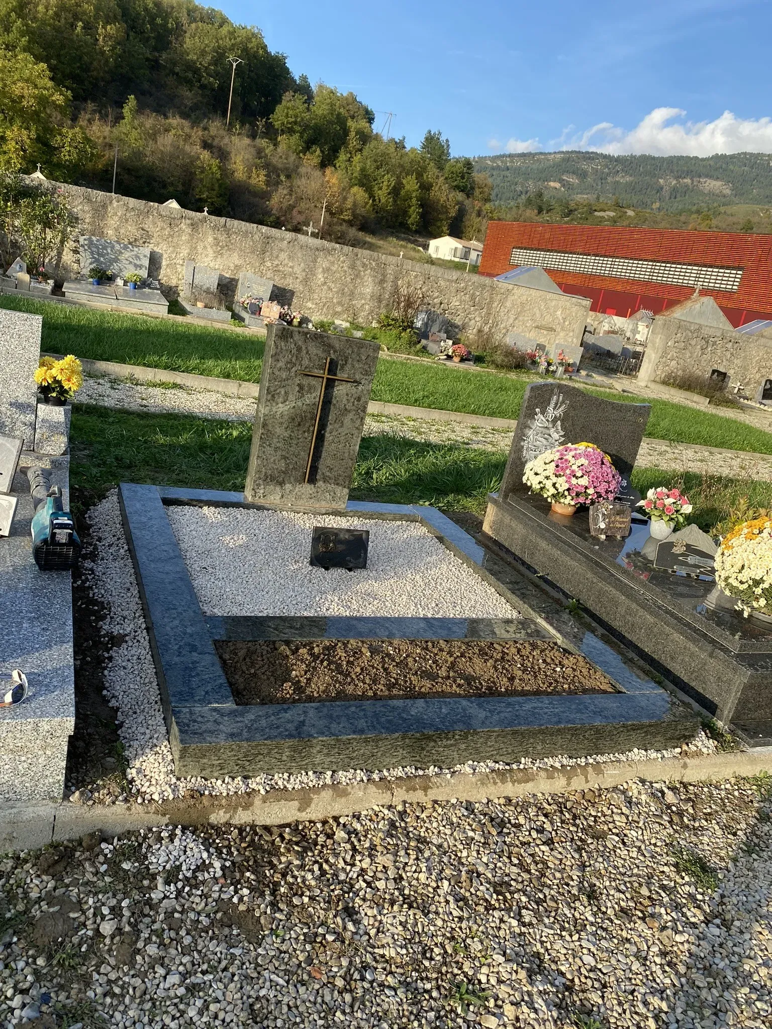 Sépulture paysagère avec stèle en granit ornée d'une croix et d'un espace végétalisé.