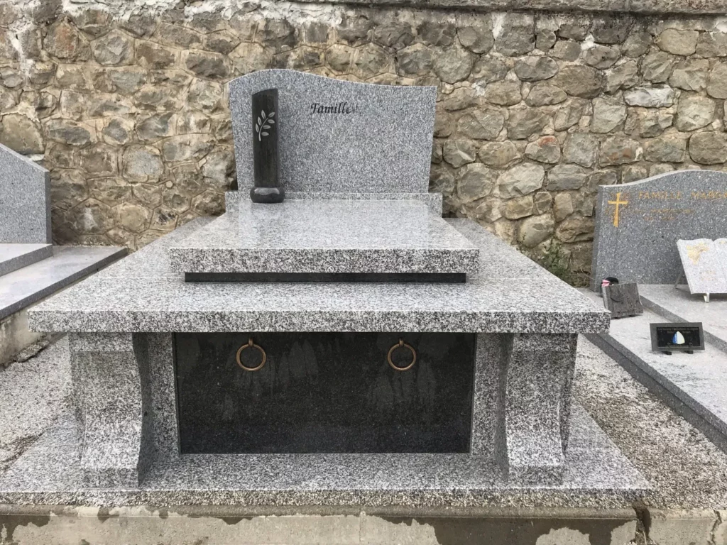 Grand caveau familial traditionnel en granit gris tacheté avec stèle ondulée.