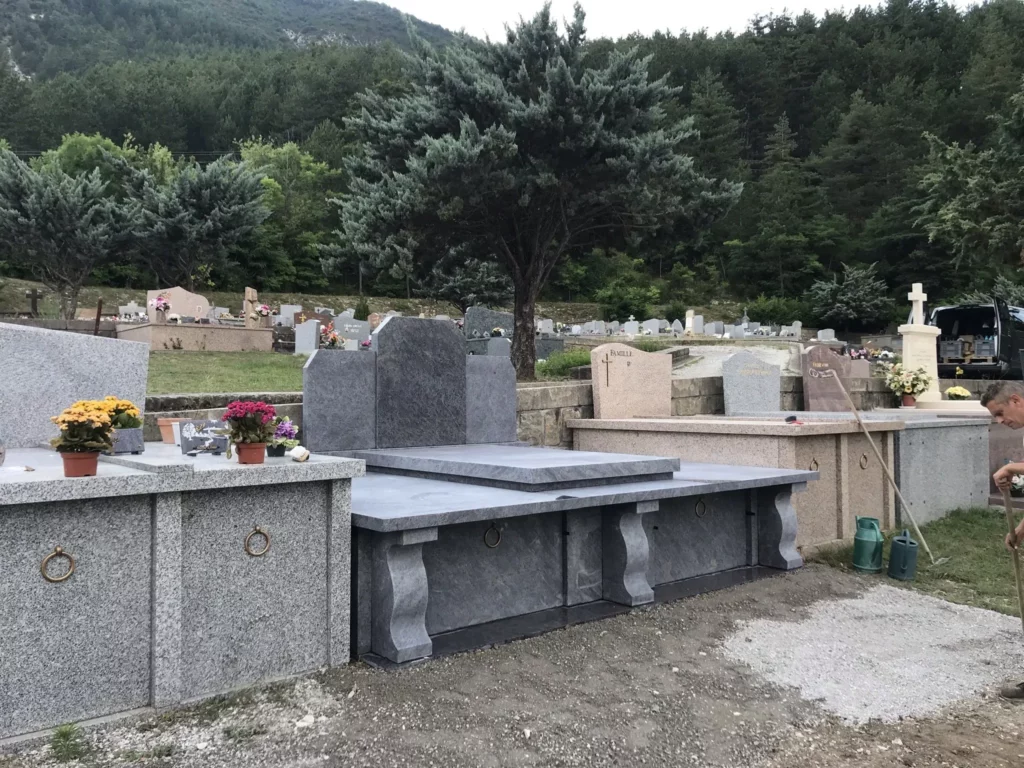 Caveau funéraire double en granit gris avec stèle dans un cimetière paysager.