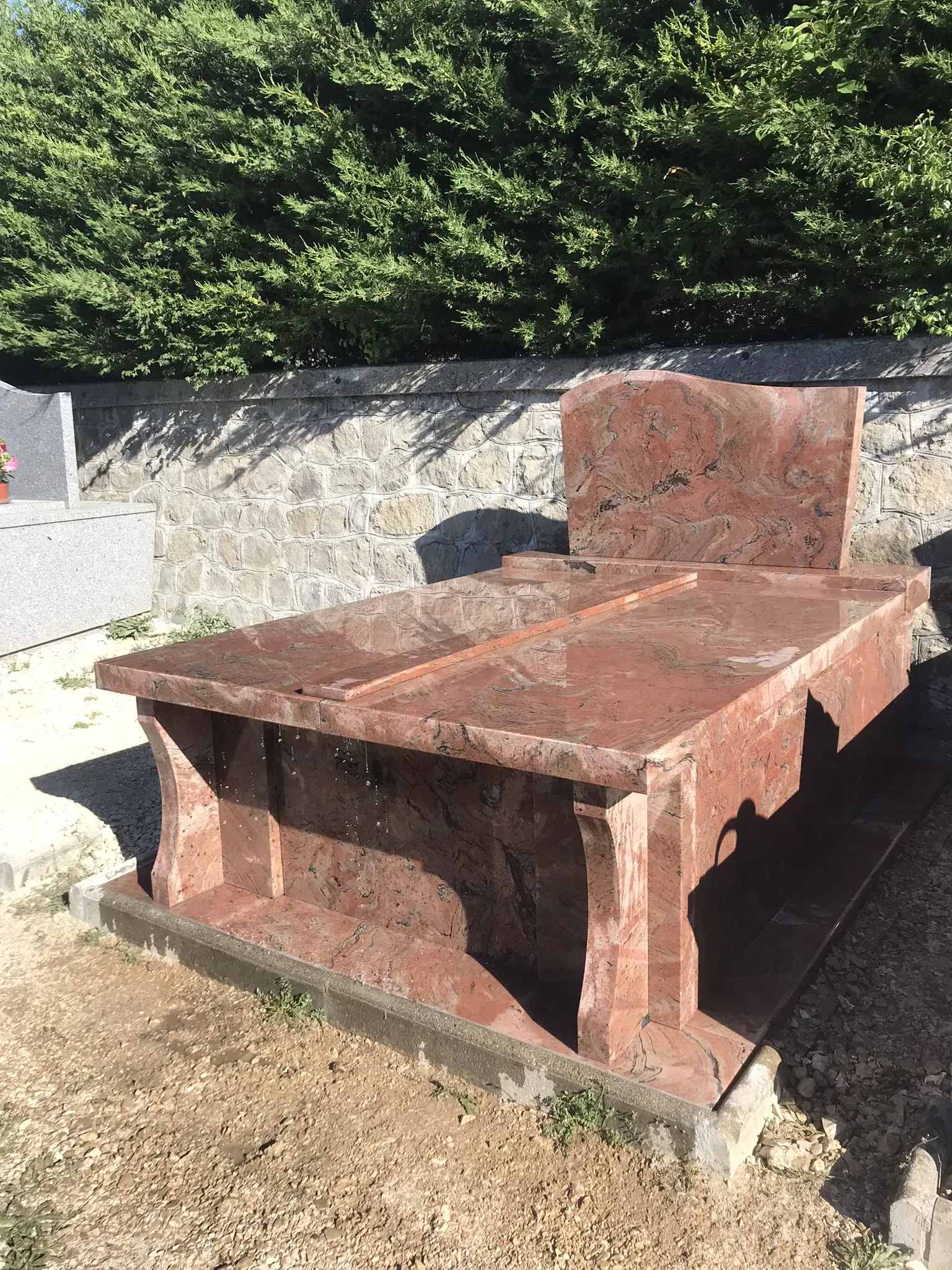 Imposant monument funéraire en granit rose et rouge veiné dans un cimetière.